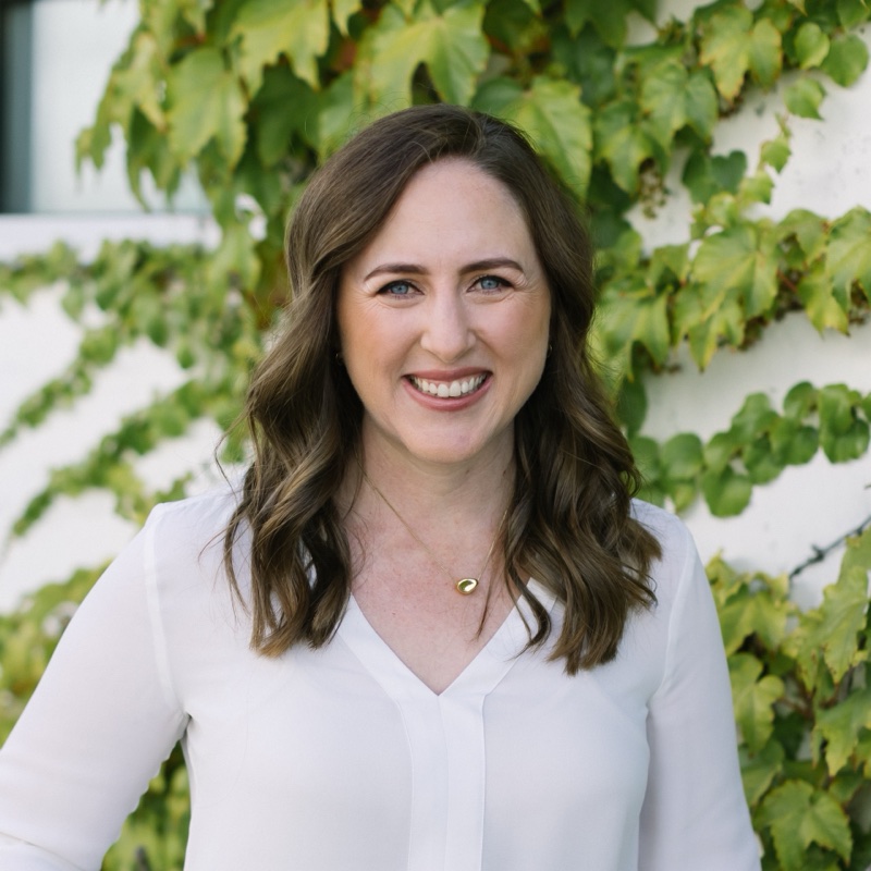 Roxanne Burbach, smiling, in front of an ivy-covered wall